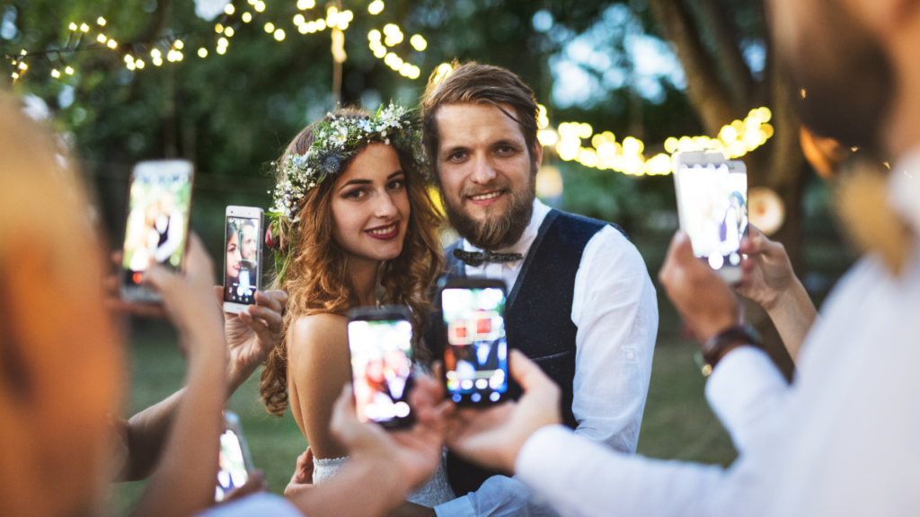 Bride and groom being photographed by guests on multiple mobile phones